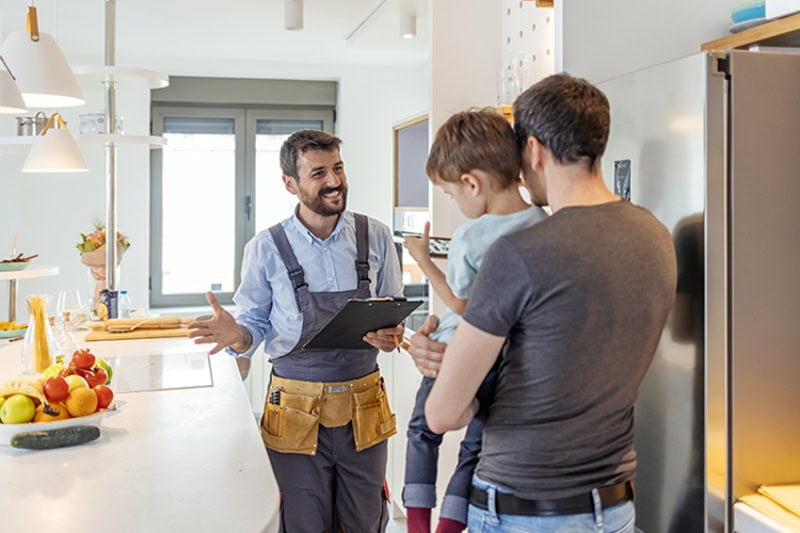 Professional plumber in uniform talking to male client and his small son indoors.