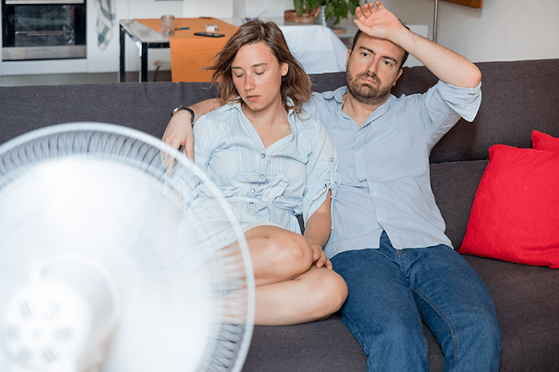 Image of couple sitting on couch in front of fan. How Can You Manage Your Home’s Humidity?